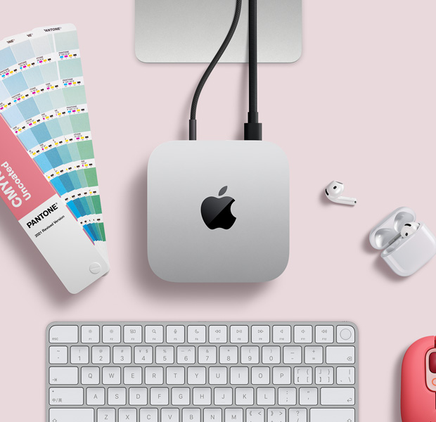 桌上的银色 Mac mini 的俯视图,设备旁边摆放着 AirPods、粉色无线键盘、粉色无线鼠标和一组呈扇形排开的色卡。